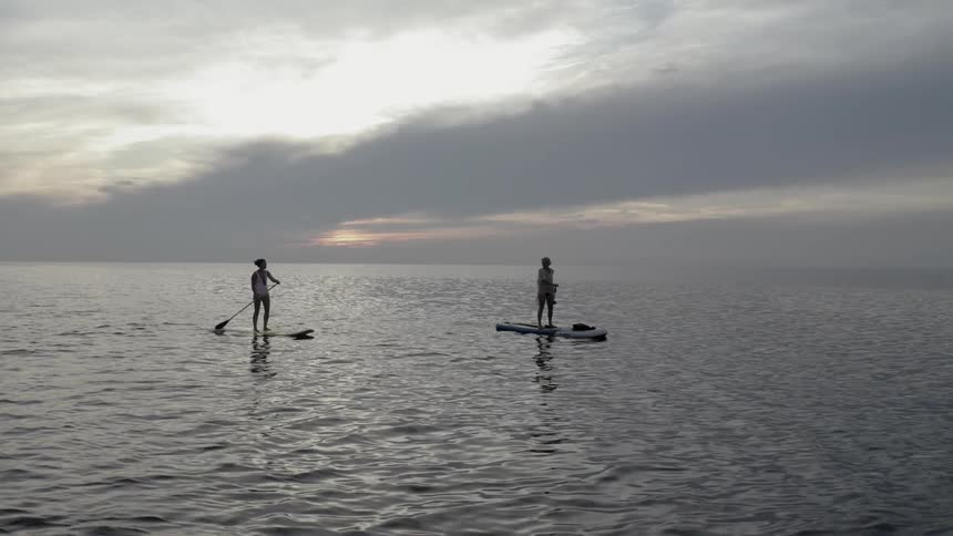 Two people standing and rowing boats on the calm ocean