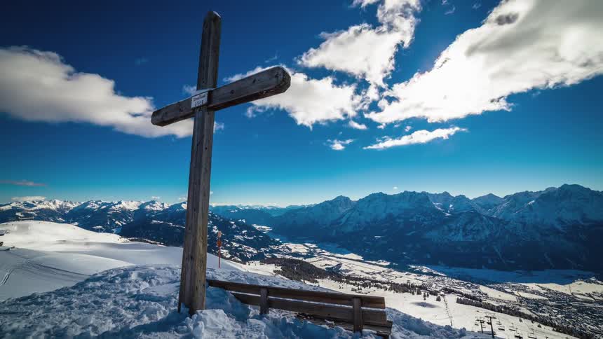 A wooden cross sticks out of the snow on the top of a hill