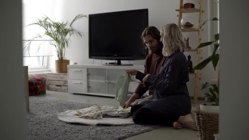 Expectant couple sit on floor examining baby clothes