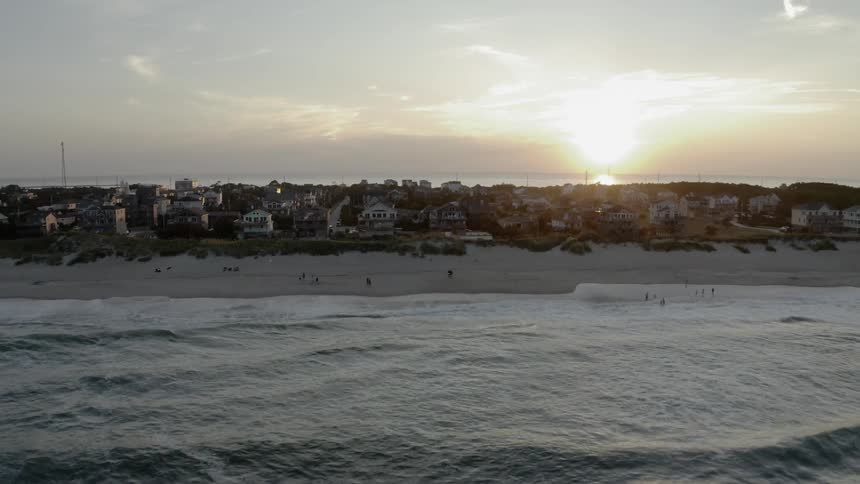 The sun sets over houses on a beach with rippling waves