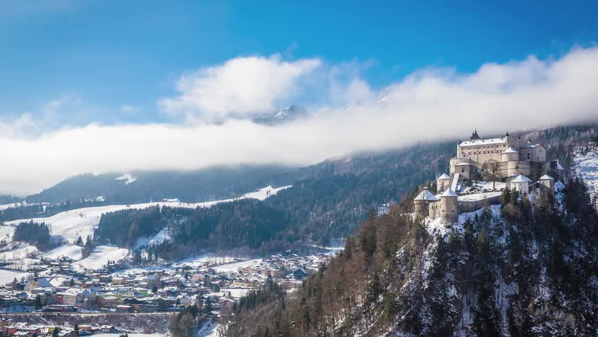A mansion sits atop a snow covered hill near a mountain range