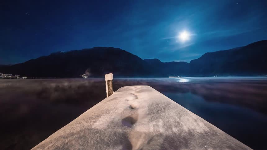 A snow covered dock along a lake surrounded by mountains