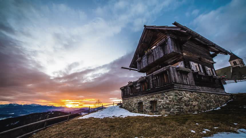 A chalet atop a snowy mountain top at sunset