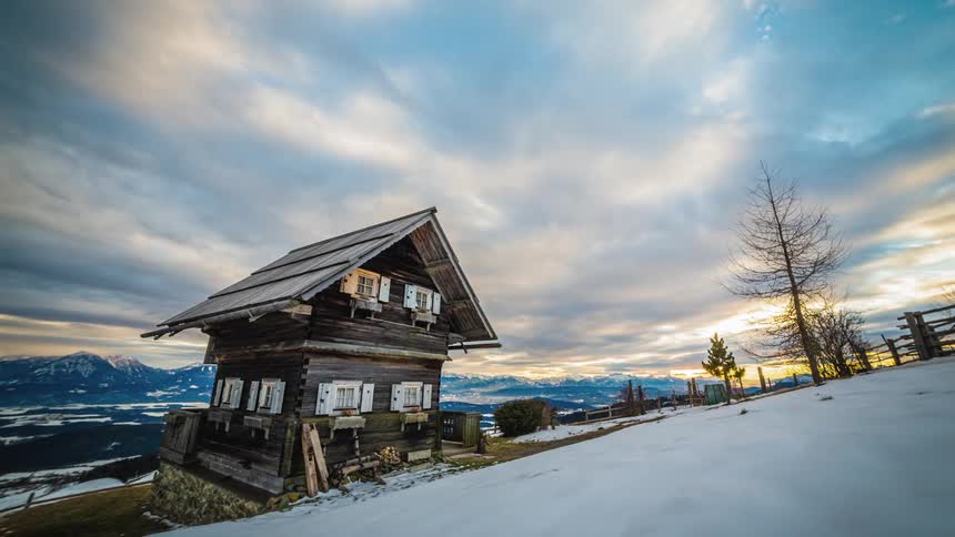 Clouds pass over wooden two story house with mountains in distance