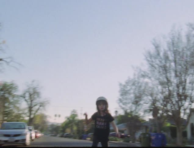 A young girl skateboarding down the road through a neighborhood