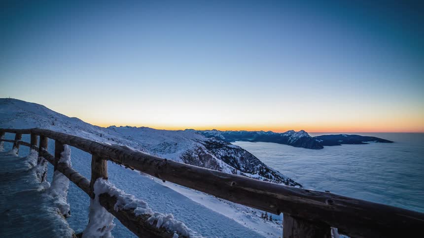 A fenced in walkway overlooks a snow covered mountain and ocean