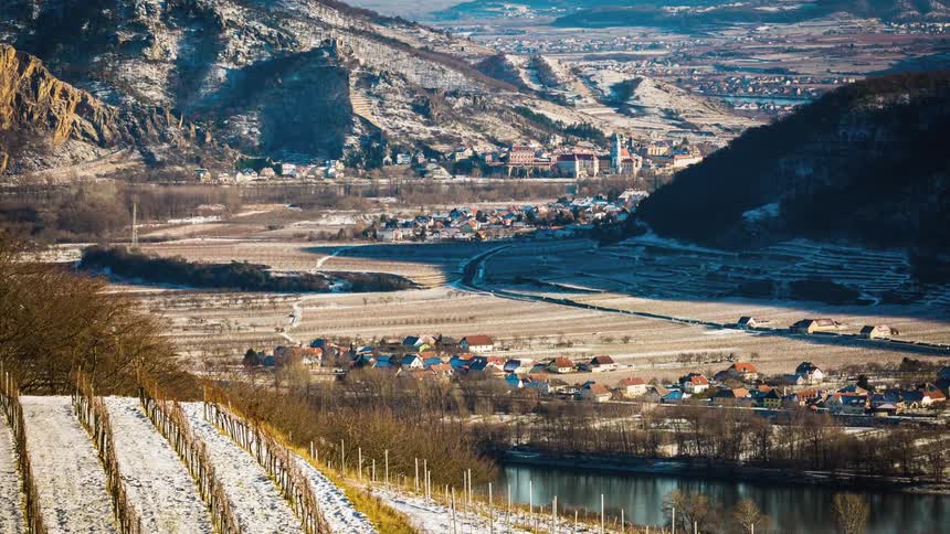 A vineyard next to a canal and a town with mountains in the background