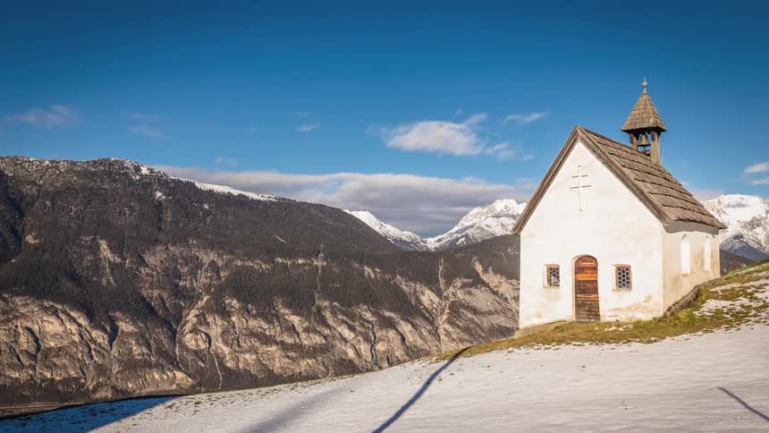 Clouds move above an old church that stands on a mountain that is part of a mountain range