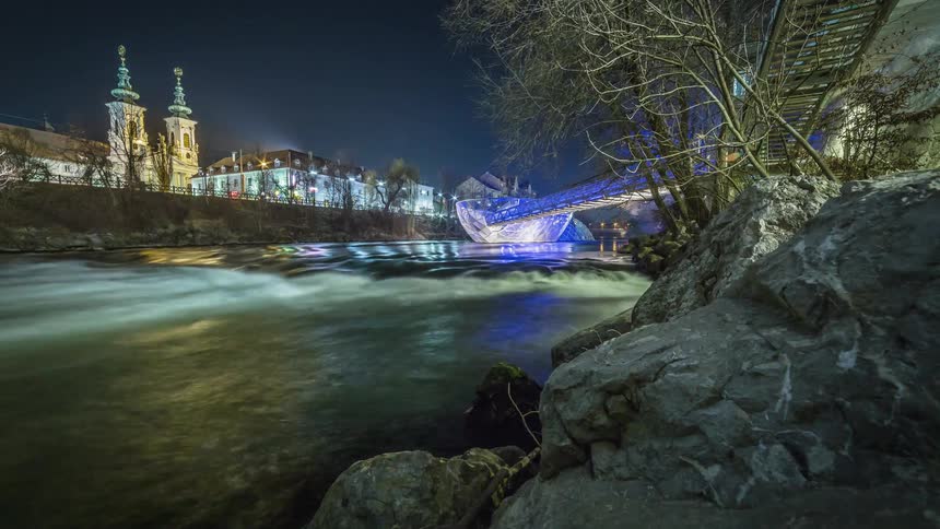 Water rushes down a river that passes through a city at night