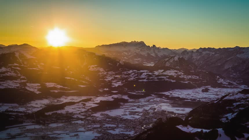 The sun rises over the mountains near the snowy fields