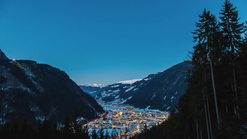 The sun sets over a city in snowy mountains