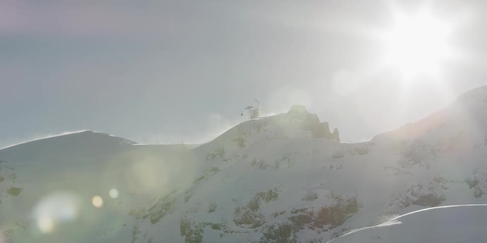 The sun glaring behind snow covered mountain peaks