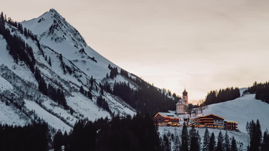 A building at the bottom of a snowy mountain ridge