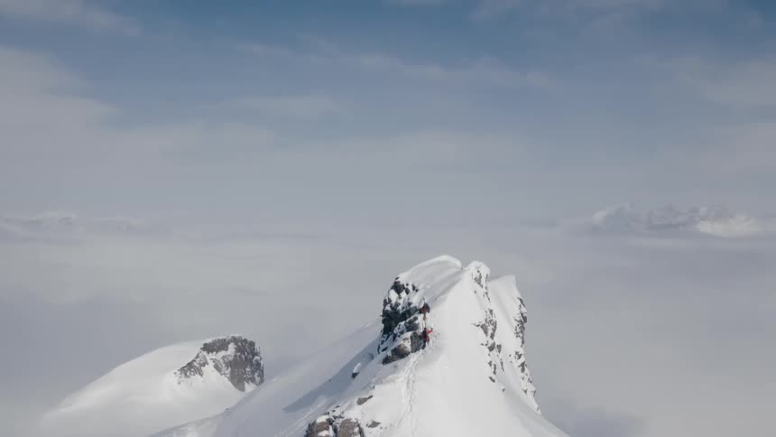 An aerial view of hikers climbing a snowy mountain peak in the wilderness