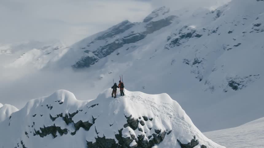 Two people holding skis stand on top of a snow covered mountain