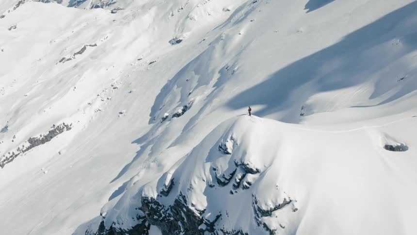 A person stand atop a snow covered mountain peak anticipating to ski down