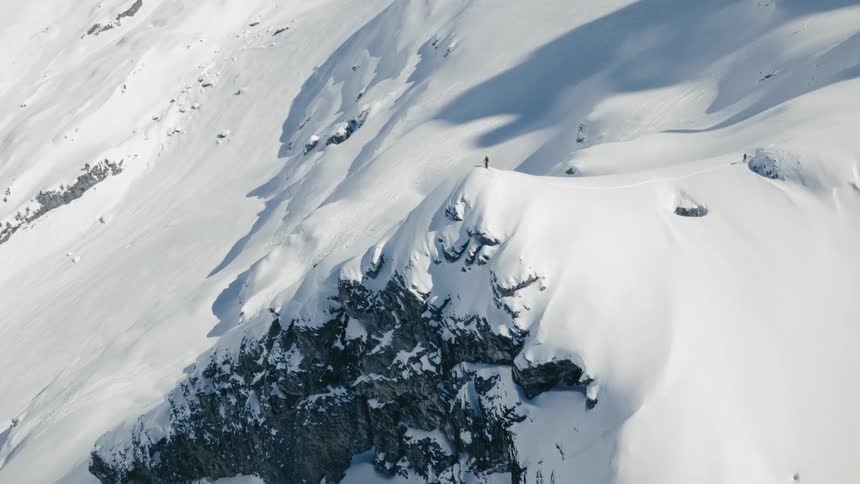 A person stands on top of a snow covered rock on a mountain side