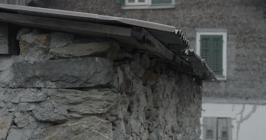 Rain drips off the metal roof of a building constructed with gray stacked stone
