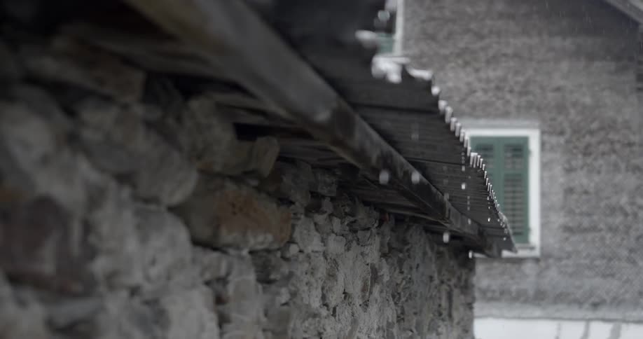 Rain drops drain off of a tin roof which extends over a stucco wall