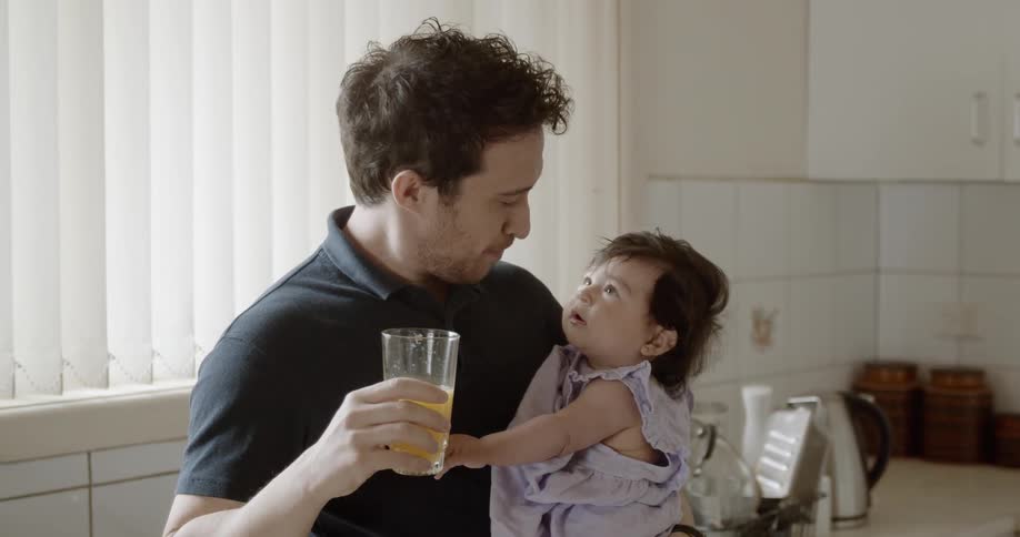 A father holds his daughter while drinking orange juice