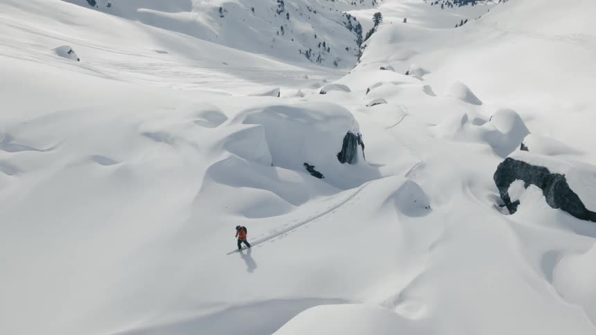 A man walks with skis on across a snow covered mountain