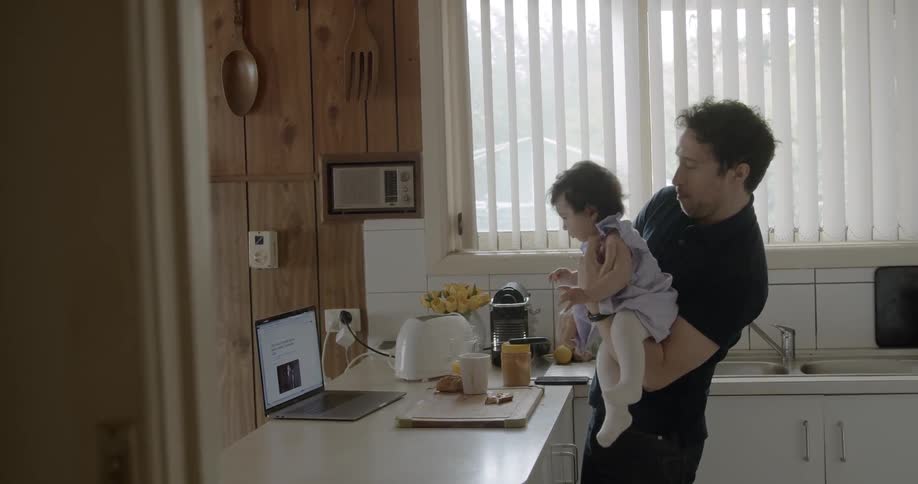 Father holding baby daughter while eating in the kitchen