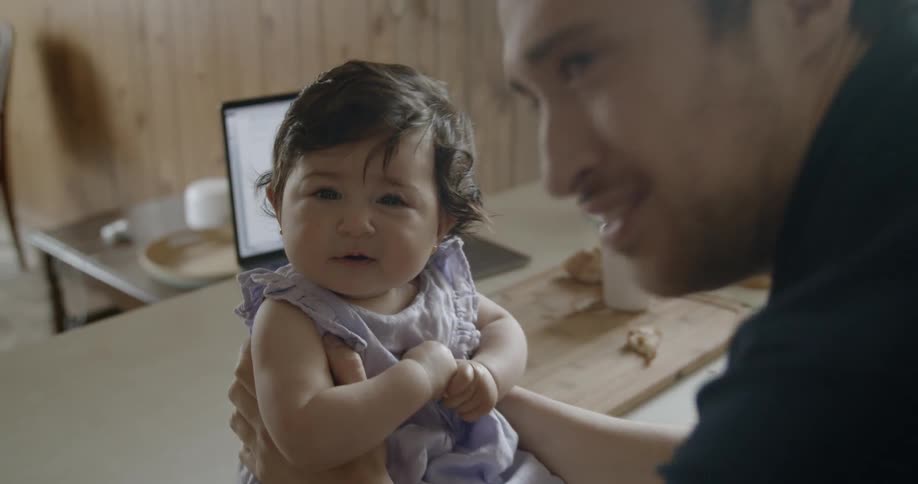 Man holds infant baby and talks to her in the kitchen during daylight