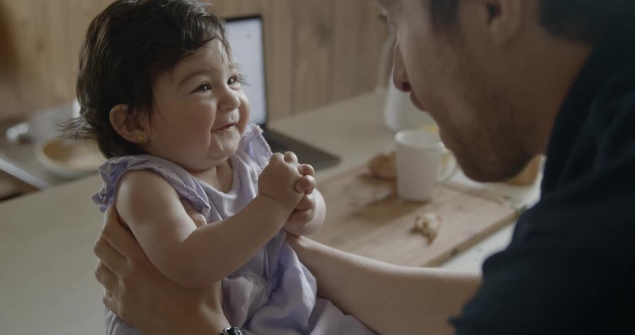A father cuddles and places his nose to that of his daughter before making her laugh by making faces