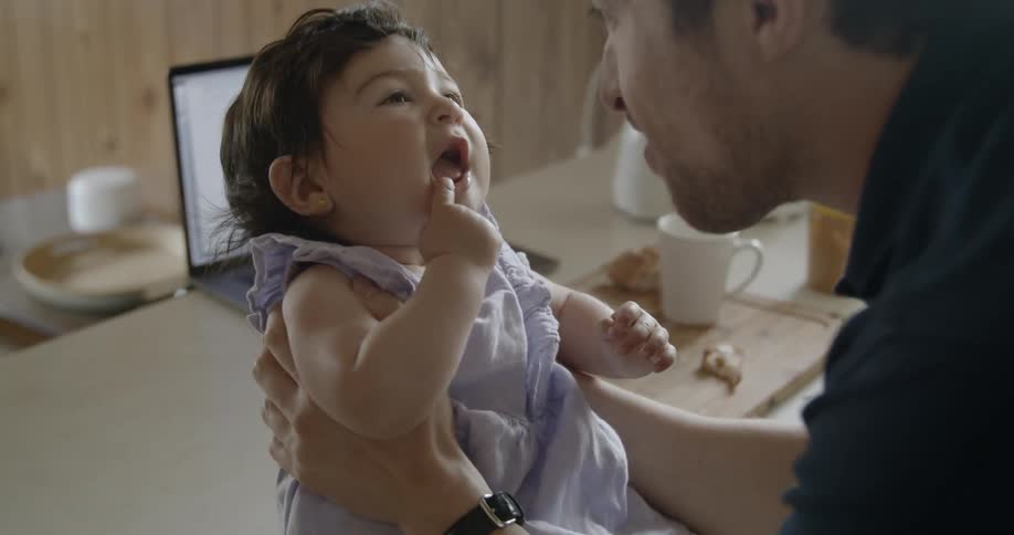 A father plays with his daughter who is sitting on the kitchen surface at breakfast