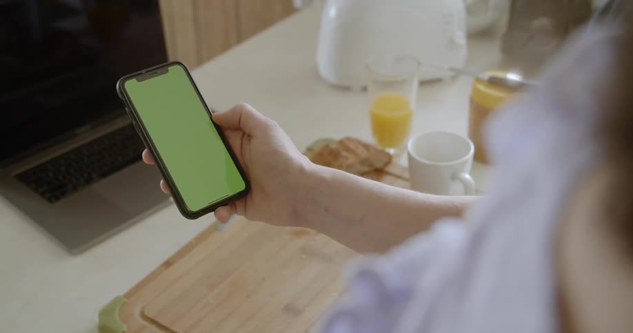 A woman holds and looks at a smartphone while having breakfast