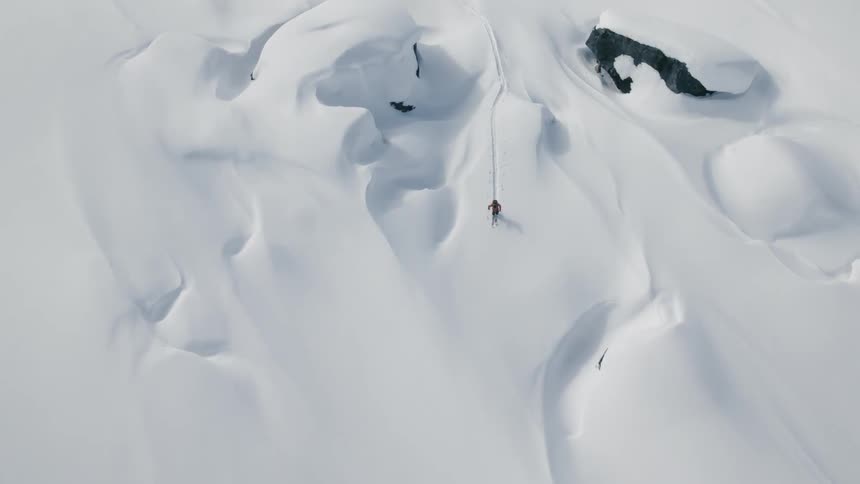An aerial view of a person wearing skis hiking across a snowy terrain