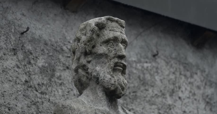 Marble worn statue of a long hair and bearded man outdoors under rain