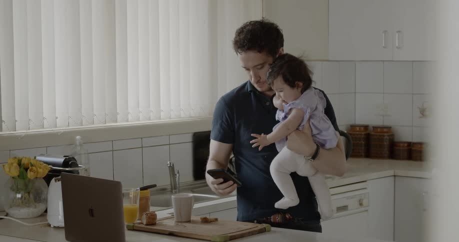 Man holding baby on kitchen while typing on phones