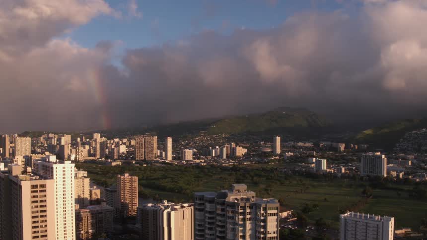 A rainbow peaks through thick clouds surrounding a city