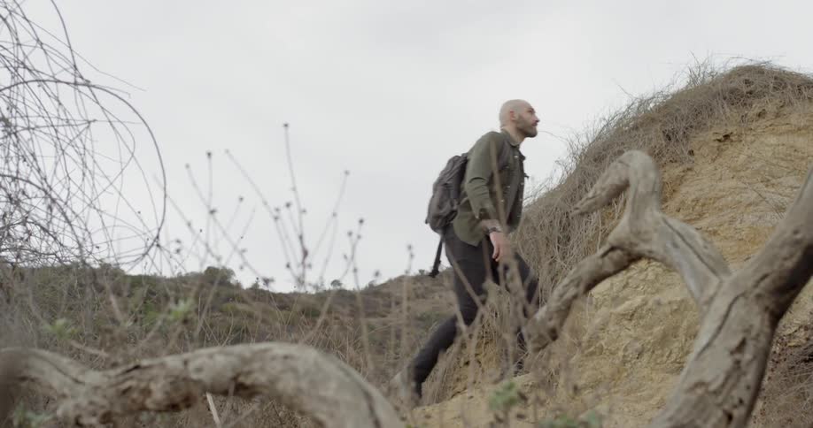 A man hikes through hills surrounded by dead plants and weeds