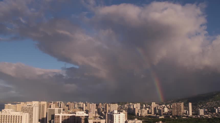 Huge clouds and a lovely rainbow are poised in the sky above a sprawling city with many tall buildings
