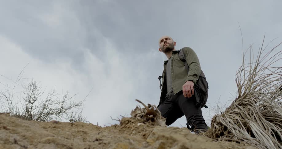 A white man stands on a hillside and looks around at his surroundings