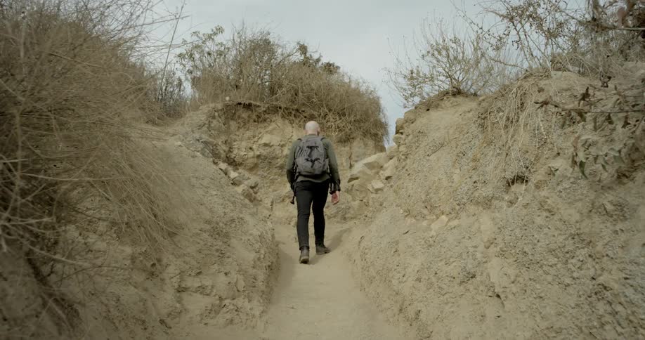 A man carrying a backpack hikes up a steep incline on a dirt trail