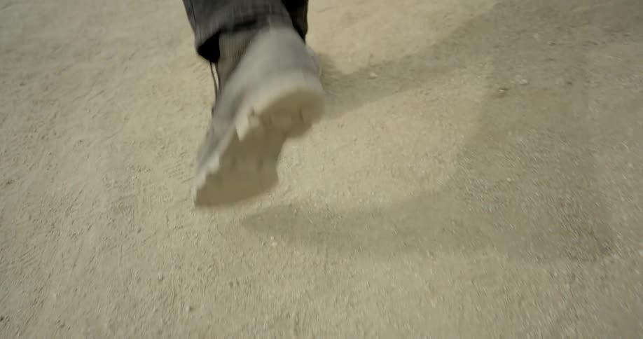 A man wearing black boots walks along a dirt path