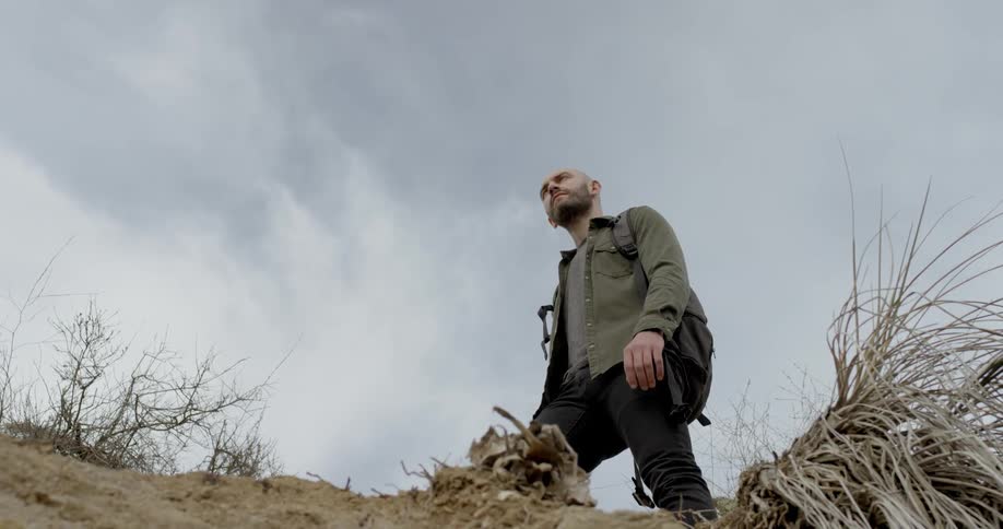 A white man stands on a hill and looks off into the distance