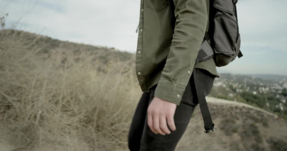 A man wearing a backpack hikes up a hillside on a cloudy day