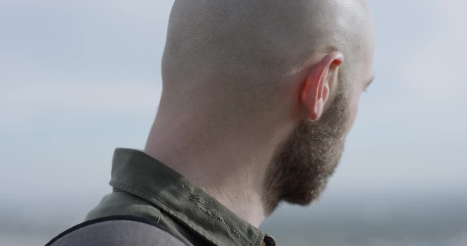 A man with a beard and shaved head looks at something in the distance