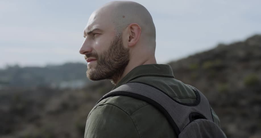 Man looks towards the left then turns his head to the right as he stands near the mountains