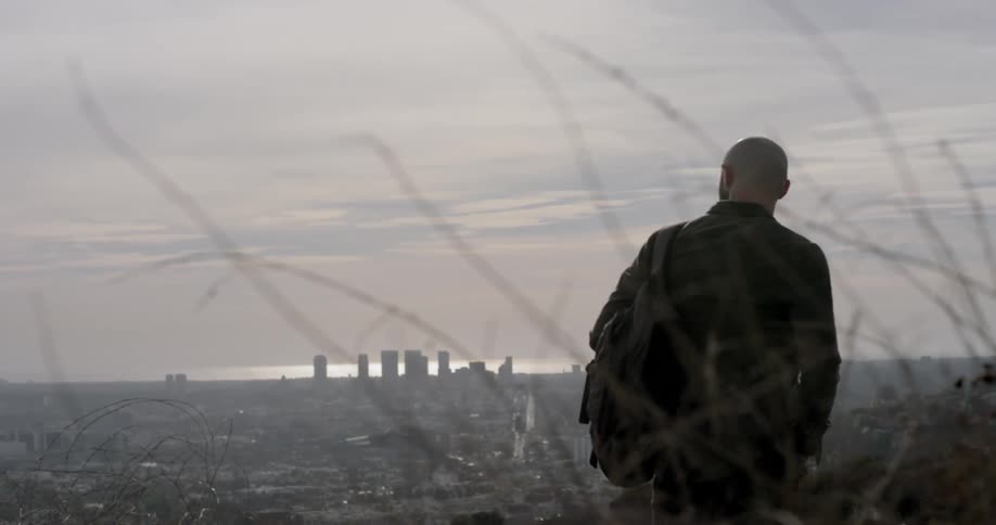 A man hikes on a hillside overlooking a city skyline