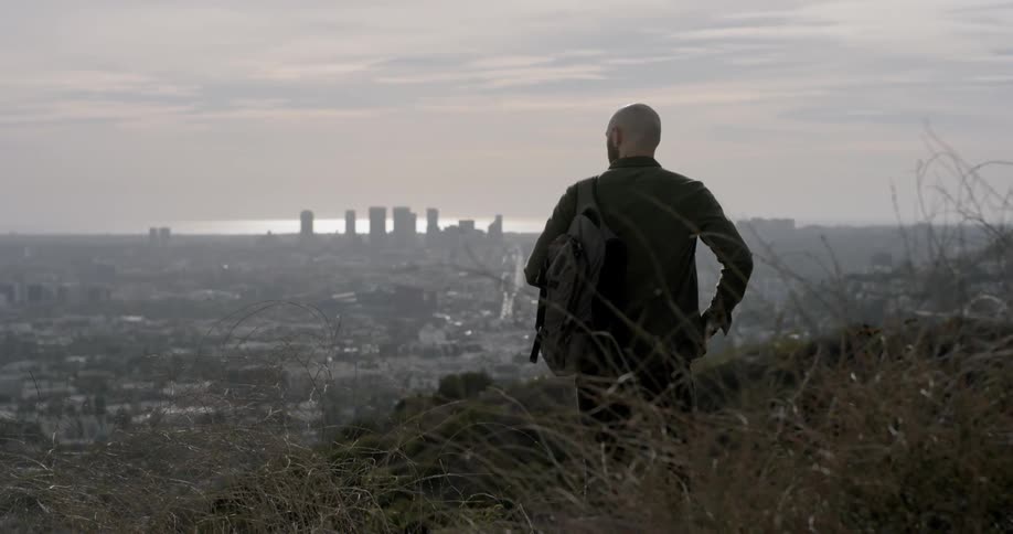 A man stands on a hill overlooking skyscrapers in the distance