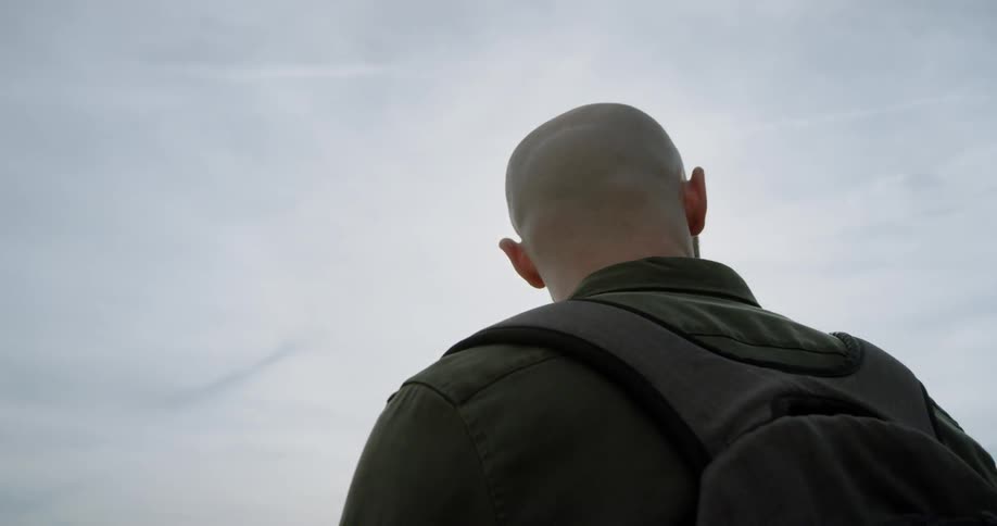 Bearded man with backpack standing outdoors at noon