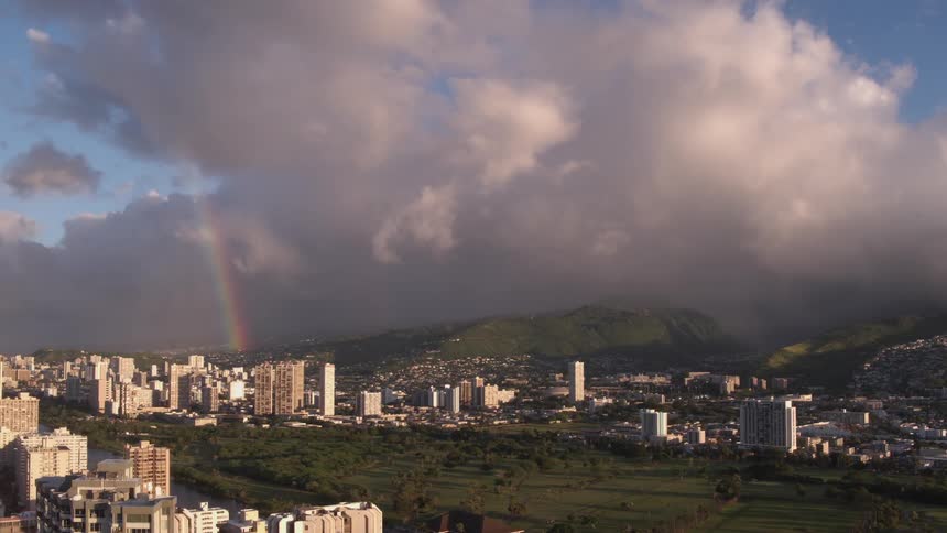 A rainbow shines through the clouds on the city and mountains in the distance