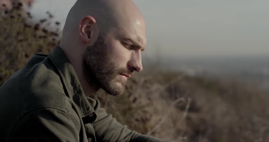Bearded man sitting outdoors looking at horizon