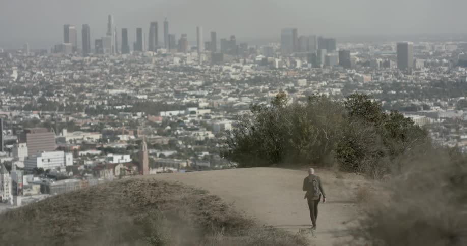 A man walks a dirt road toward a large city