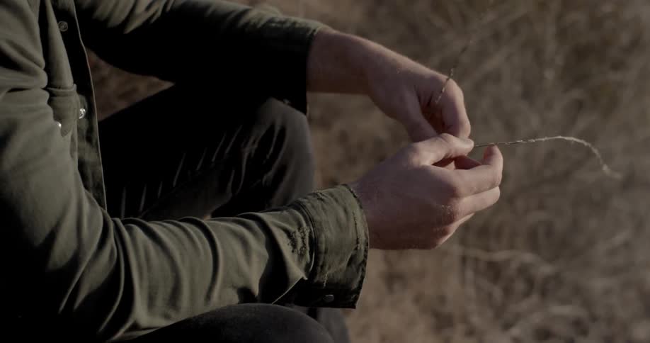 A person sitting outdoors fiddling with a long stalk of grass